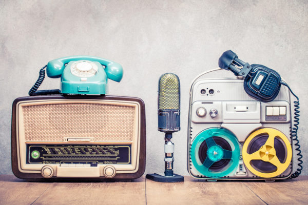 Retro broadcast radio, telephone, reel to reel tape recorder circa 60s, microphone, headphones on wooden table front concrete wall background. Vintage style filtered photo Crown SXSW